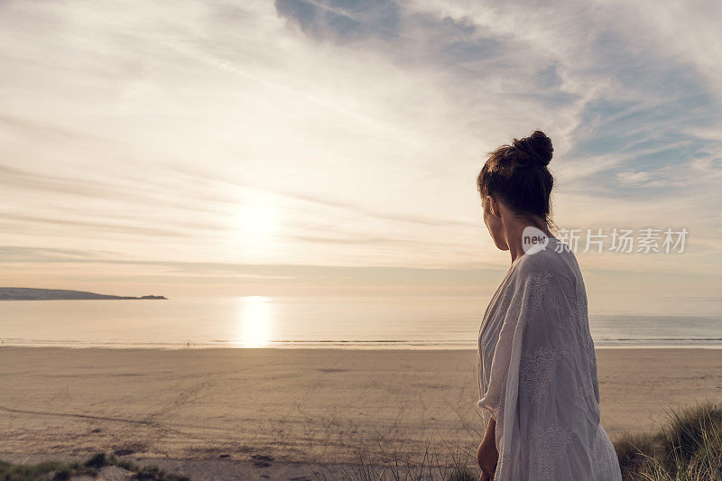 一名女子站在英国康沃尔郡Gwithian Towans海滩的沙丘上，享受着夏末的阳光。